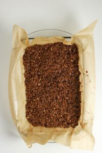 A baking tray lined with parchment paper holds a rectangular block of chocolate rice crispy treats.