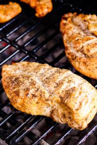 Seasoned chicken breasts cooking on a grill grate over hot coals.