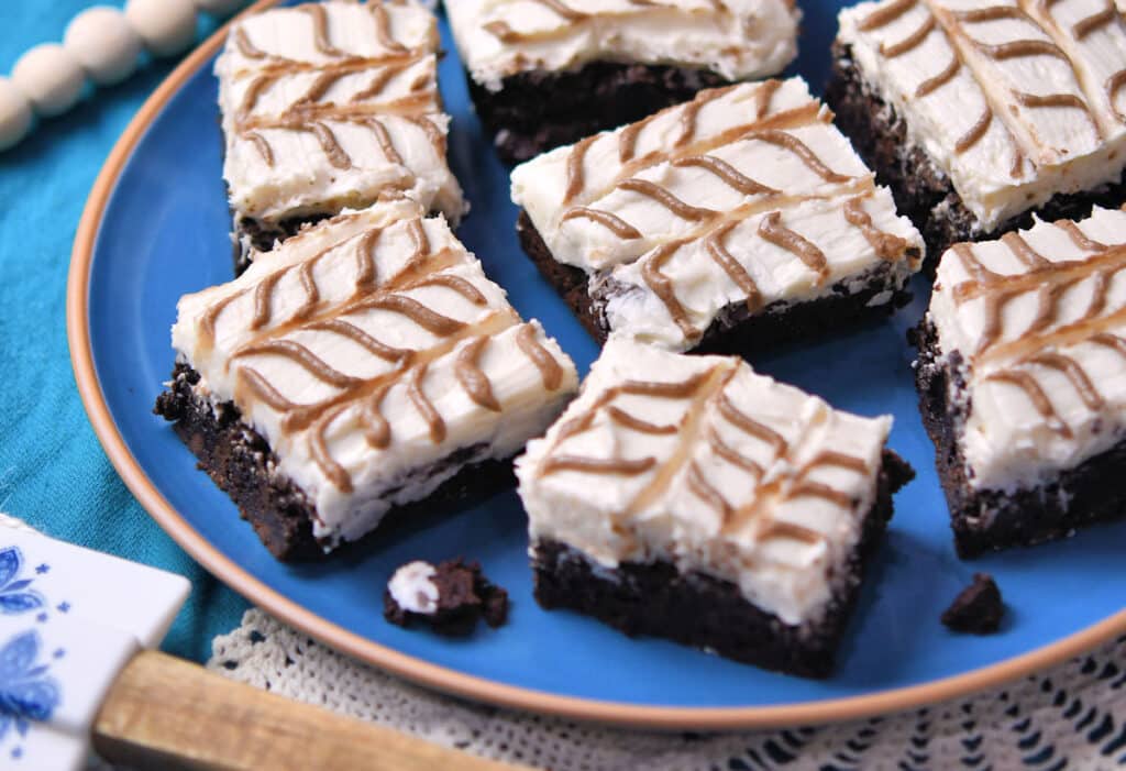 Brownie squares topped with white frosting and chocolate swirl designs are arranged on a blue plate.