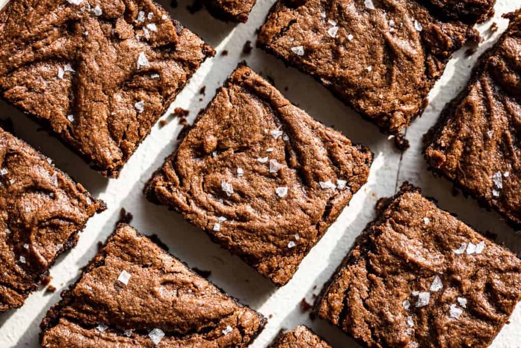 Close-up of several chocolate brownies arranged in rows, topped with a sprinkling of coarse sea salt.