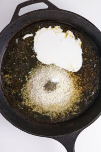Uncooked rice, cream, broth, pepper, and oil in a cast iron skillet, ready to be mixed and cooked.