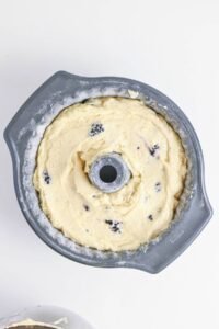 Bundt pan filled with unbaked cake batter containing visible dark berries on a white surface.