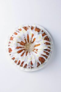 A bundt cake with white icing drizzled on top, served on a white plate against a white background.
