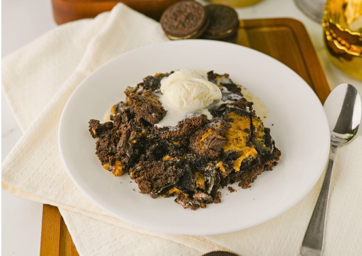 A dessert of chocolate and peanut butter cake topped with a scoop of vanilla ice cream is served on a white plate with a spoon and napkin.