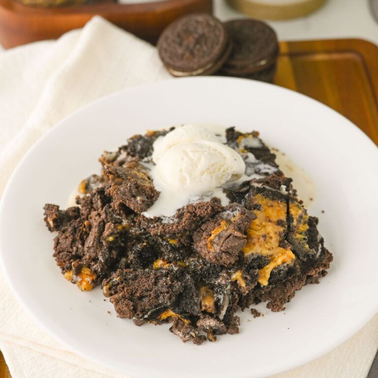 A plate of chocolate Oreo dessert topped with a scoop of vanilla ice cream on a white plate, with whole Oreo cookies in the background.