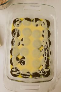 A glass baking dish with a layer of chocolate sandwich cookies partially covered in a yellow custard-like liquid.