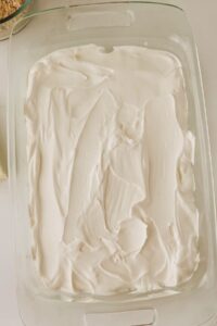A glass baking dish filled with an even layer of white whipped topping, with some utensil marks visible on the surface.