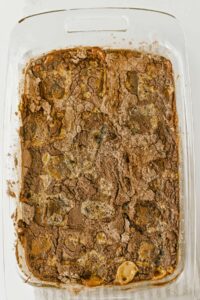 A glass baking dish filled with a baked chocolate dessert featuring a cracked, textured surface and visible patches of melted chocolate.