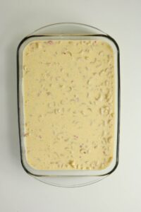A glass baking dish filled with an uncooked macaroni and cheese mixture, viewed from above on a white surface.