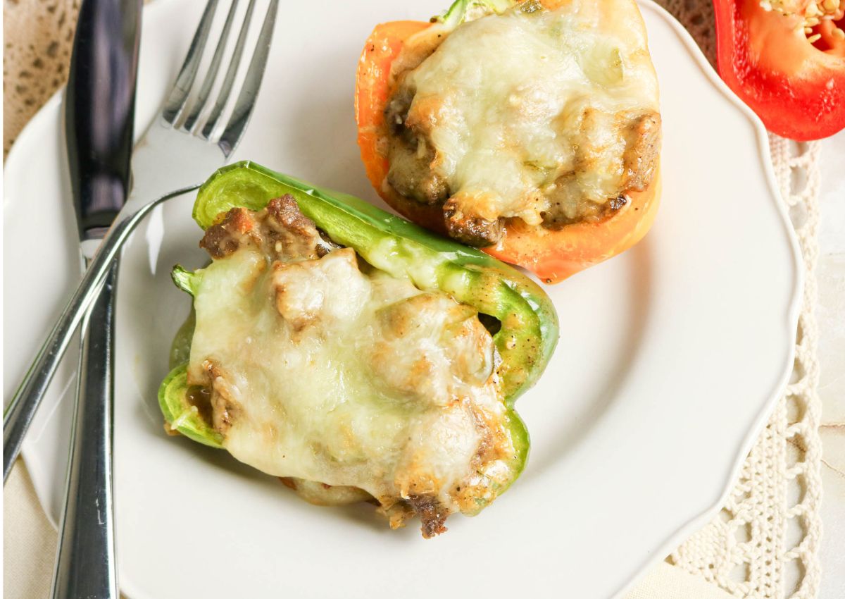 A white plate with two stuffed bell pepper halves topped with melted cheese, next to a fork and knife on a lace tablecloth.