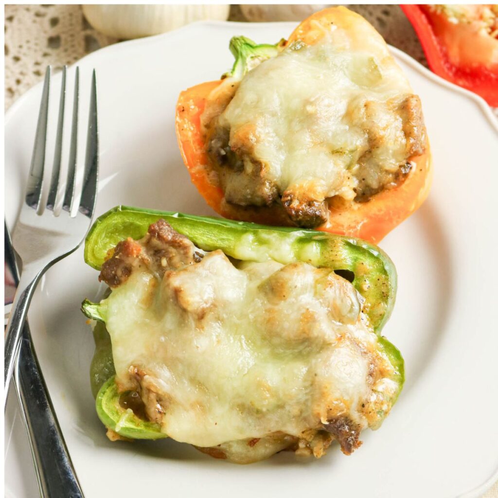 Two stuffed bell pepper halves topped with melted cheese on a white plate, served with a fork.