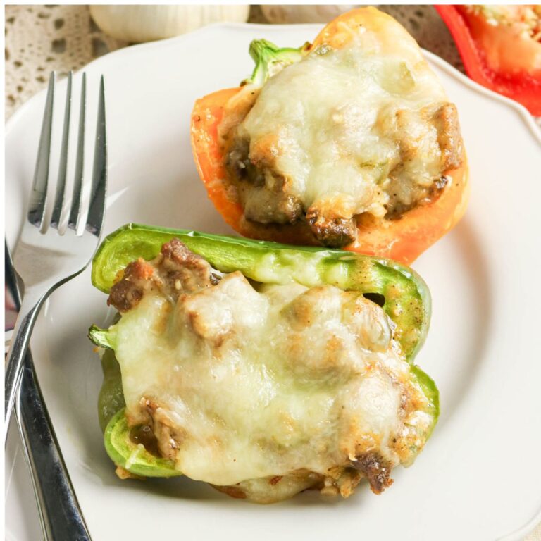 Two stuffed bell pepper halves topped with melted cheese on a white plate, served with a fork.