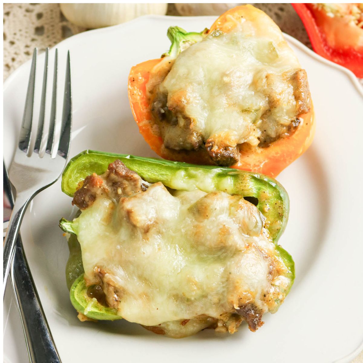 Two stuffed bell pepper halves topped with melted cheese on a white plate, served with a fork.