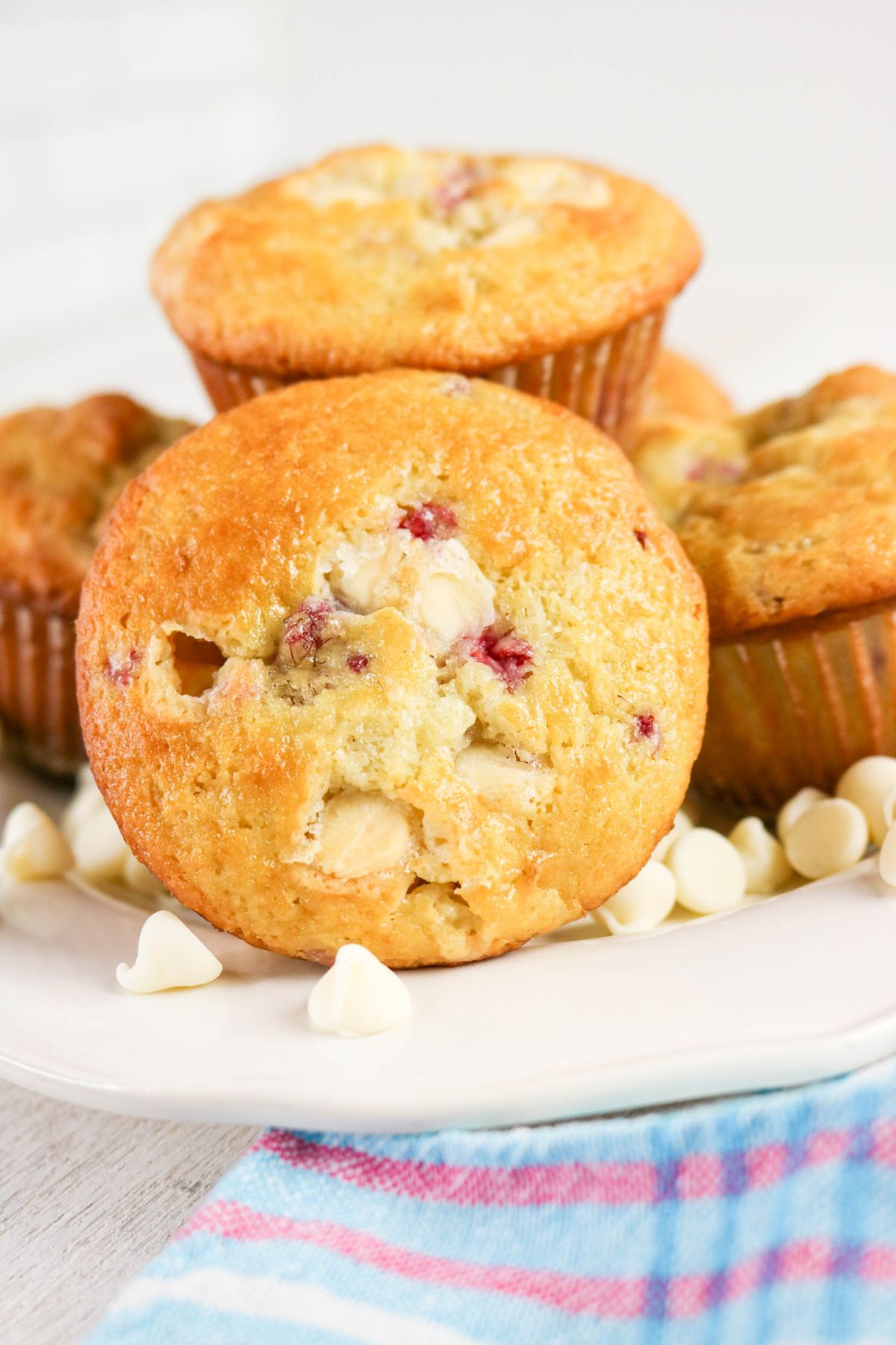 A plate of golden muffins with visible white chocolate chips and cranberries, surrounded by a few loose white chocolate chips.
