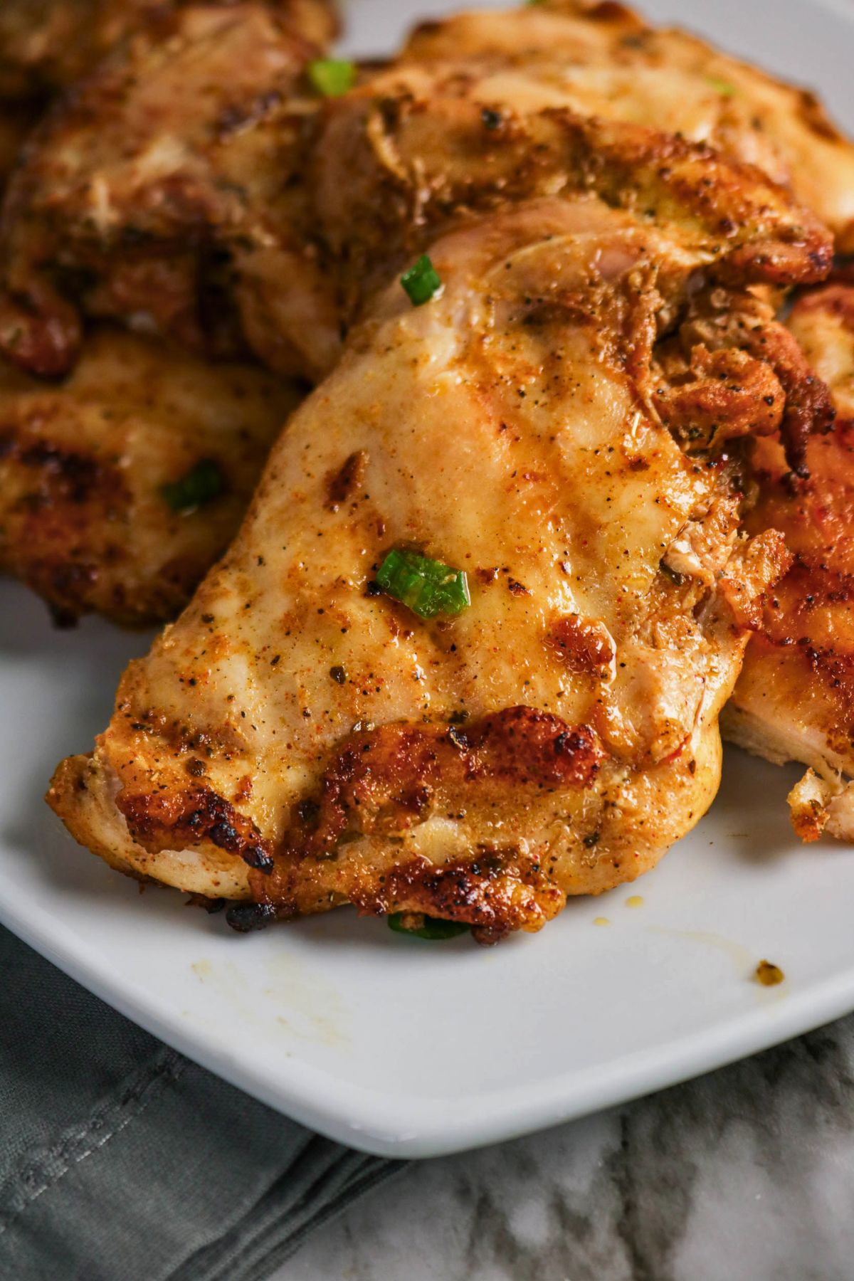 Grilled, seasoned chicken breasts with visible herbs and spices are served on a white plate alongside tender grilled boneless chicken thighs.