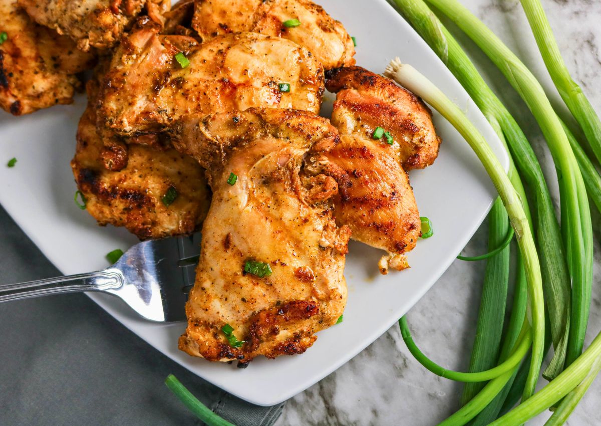 Grilled Boneless Chicken Thighs served on a white plate with chopped green onions, alongside fresh whole green onions on a marble surface.