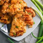 Grilled Boneless Chicken Thighs garnished with chopped green onions on a white plate, served alongside fresh green onions on a marble surface.