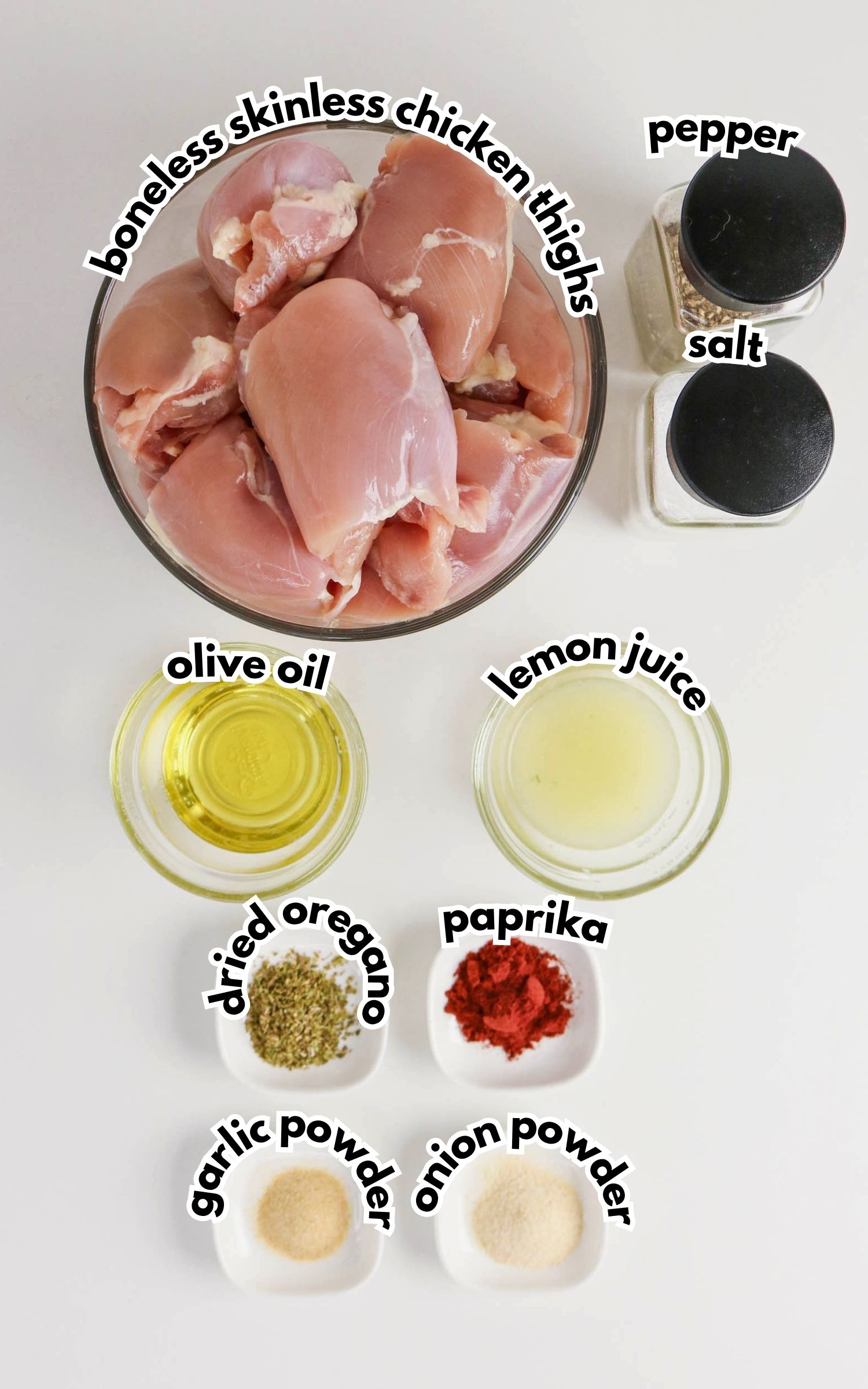 A bowl of boneless skinless chicken thighs, perfect for Grilled Boneless Chicken Thighs, surrounded by containers of salt, pepper, olive oil, lemon juice, dried oregano, paprika, garlic powder, and onion powder.