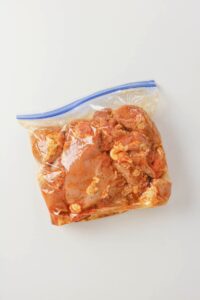 Raw marinated Grilled Boneless Chicken Thighs in a sealed plastic ziplock bag rest on a white surface.