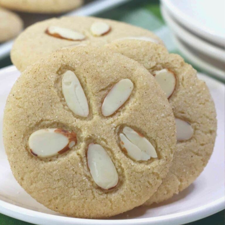 Three round cookies topped with sliced almonds arranged in a flower pattern, displayed on a white plate.