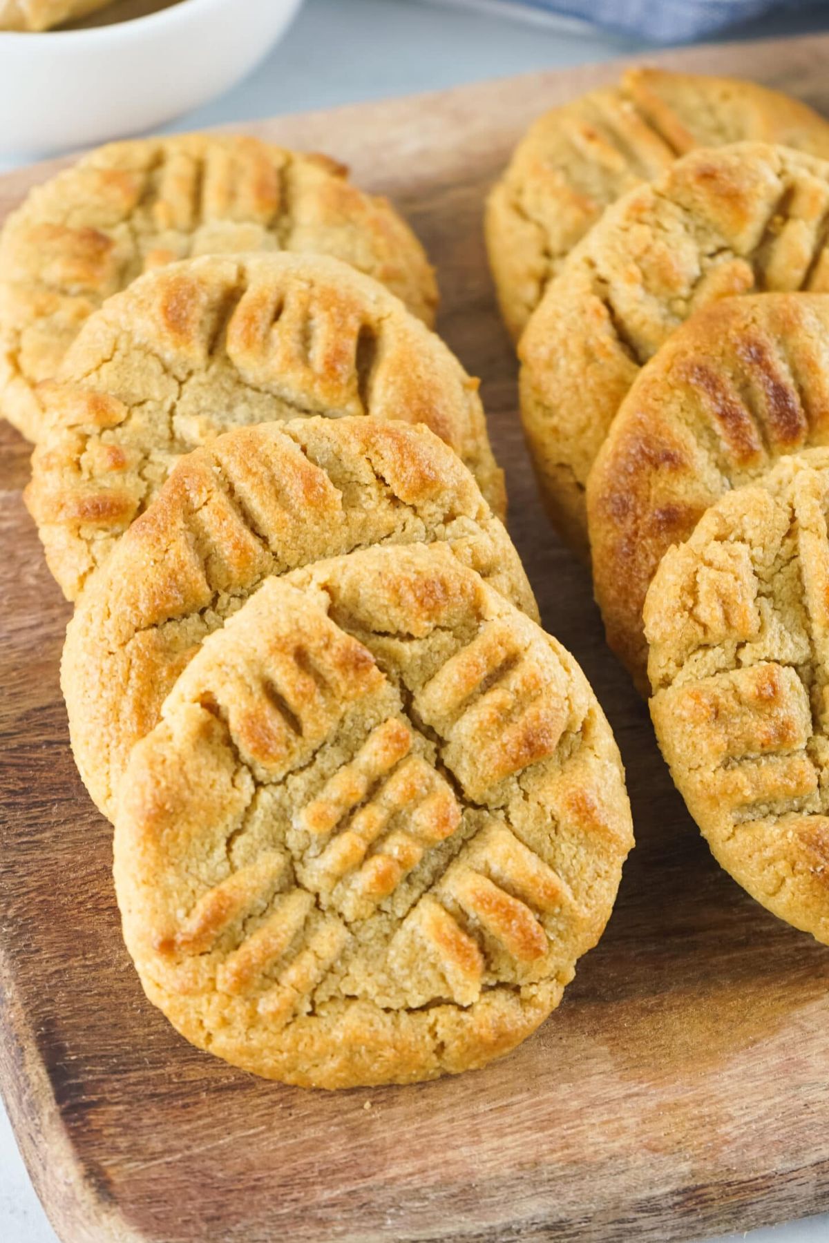 A row of peanut butter cookies with a crisscross fork pattern on top, arranged on a wooden cutting board.