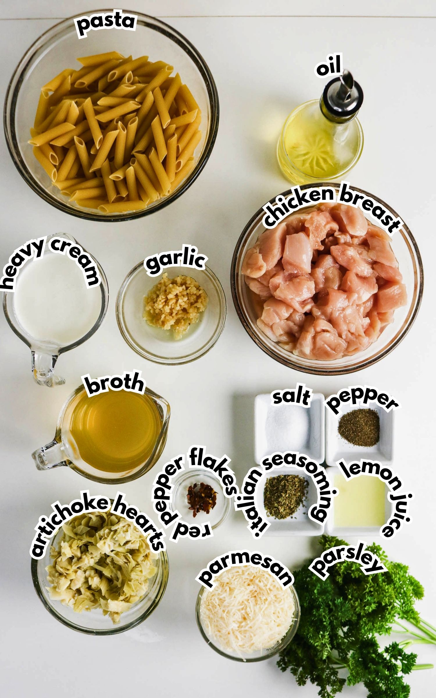 Ingredients for a pasta dish arranged on a white surface, including pasta, chicken breast, oil, cream, broth, garlic, artichoke hearts, parmesan, parsley, and seasonings.