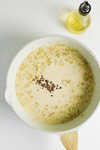 A white pan filled with a creamy soup mixture and red pepper flakes sits on a white surface next to a small glass container of oil.