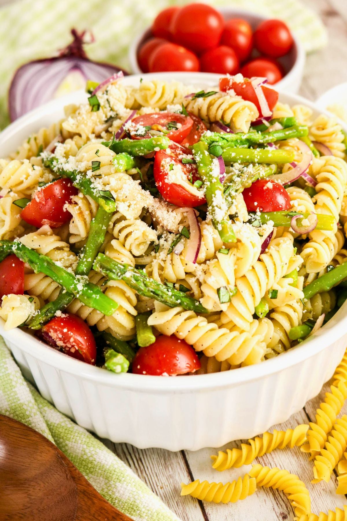 A white bowl filled with rotini pasta salad, featuring green beans, cherry tomatoes, sliced red onion, and sprinkled with grated cheese.
