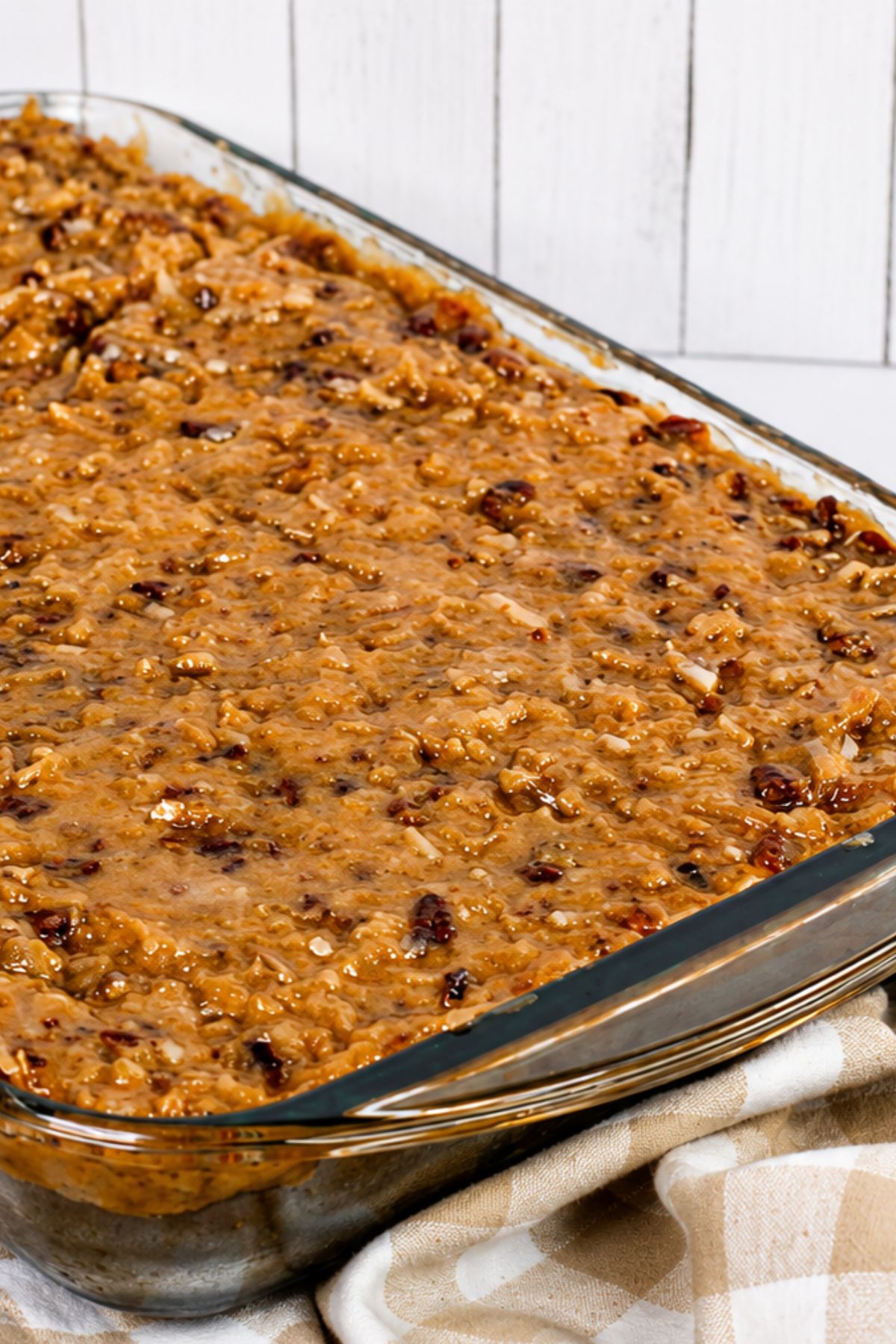 A glass baking dish filled with baked oatmeal containing oats and dried fruit, resting on a beige and white towel.