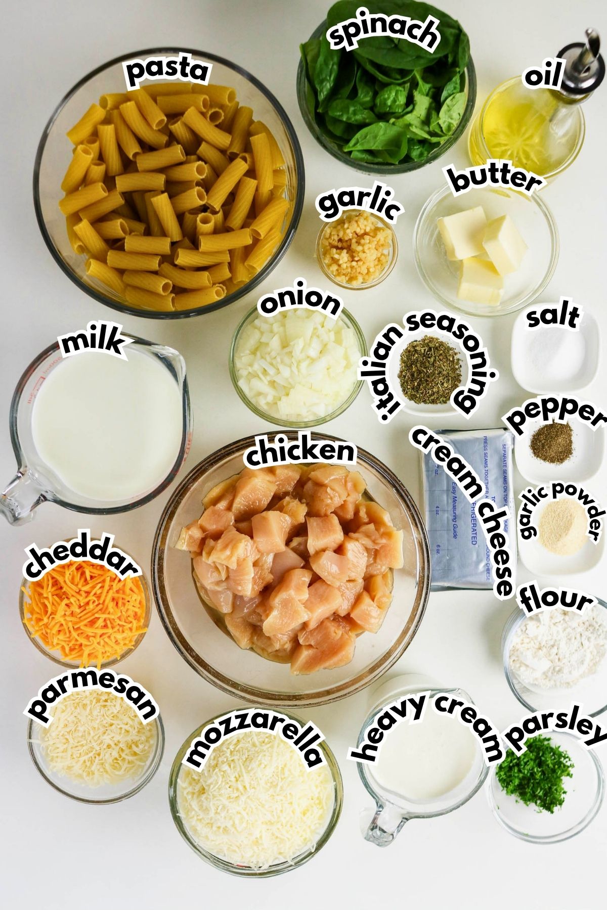 Top-down view of neatly arranged ingredients for a creamy chicken pasta dish, including pasta, spinach, chicken, cheeses, milk, cream, butter, onion, garlic, oil, seasonings, and parsley.
