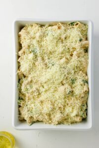 A white rectangular baking dish filled with an unbaked casserole topped with shredded cheese, shot from above.