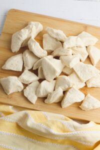 Chunks of raw biscuit dough scattered on a wooden cutting board, with a yellow and white striped cloth underneath.