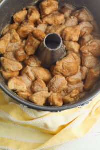 A Bundt pan filled with unbaked pieces of dough coated in cinnamon sugar, resting on a yellow-striped cloth.
