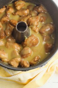 A bundt pan filled with unbaked monkey bread dough pieces coated in a yellow sauce, resting on a yellow kitchen towel.