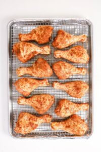 Raw, seasoned chicken drumsticks and thighs arranged on a wire rack over a foil-lined baking sheet, ready for cooking.