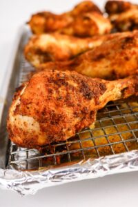 Several seasoned and baked chicken drumsticks rest on a wire rack over a foil-lined baking sheet.