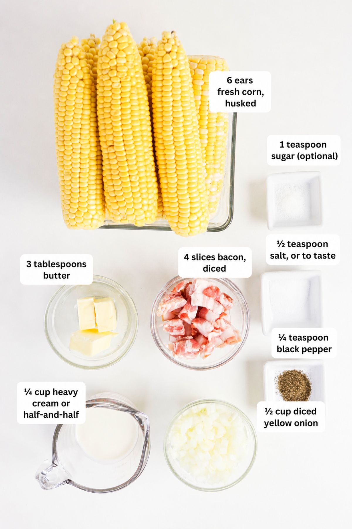 Ingredients for a corn chowder recipe, including fresh corn, bacon, diced onion, butter, heavy cream, sugar, salt, and black pepper arranged on a white surface.
