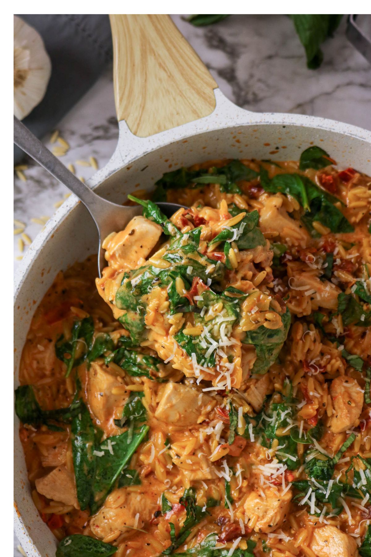 A pan of creamy chicken and spinach pasta with shredded cheese on top, stirred with a wooden spoon.