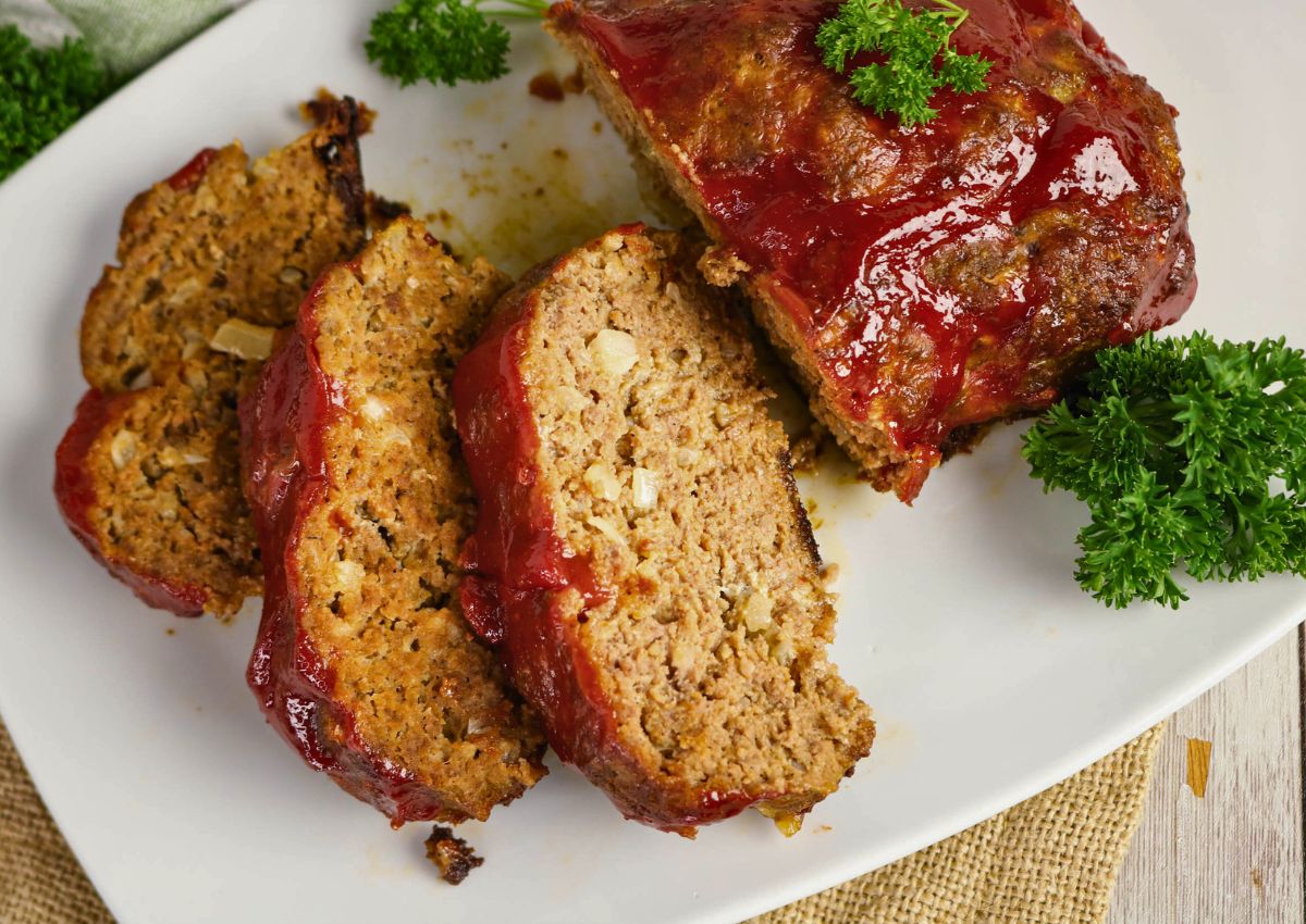 Sliced meatloaf with a ketchup glaze on a white plate, garnished with fresh parsley.