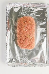Uncooked meatloaf mixture shaped into a loaf sits on a foil-lined baking sheet.