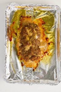 A cooked meatloaf sits on a foil-lined baking tray with browned edges and visible juices.