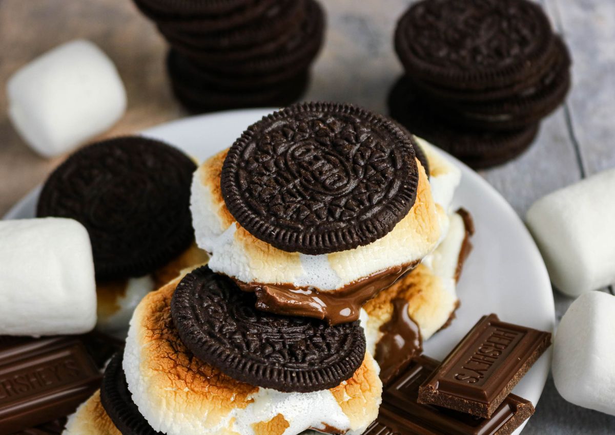 A plate with Oreo cookies, toasted marshmallows, melted chocolate, and Hershey’s chocolate pieces, surrounded by more Oreos and marshmallows.