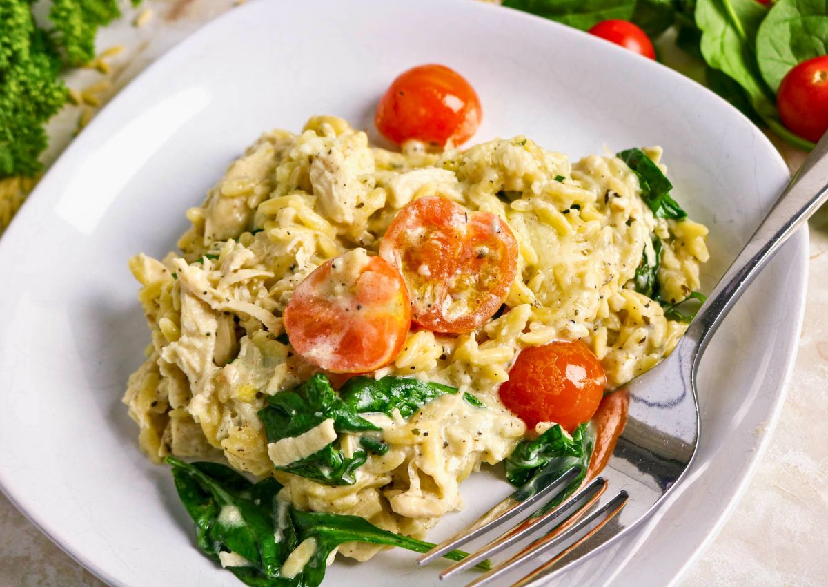 A white plate with creamy pasta, shredded chicken, cherry tomato halves, and spinach, with a fork on the side.