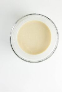 A clear glass bowl filled with a smooth, light beige batter sits on a white surface.