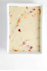 Rectangular white dish filled with a creamy batter containing visible pieces of fruit, likely prepared for baking.