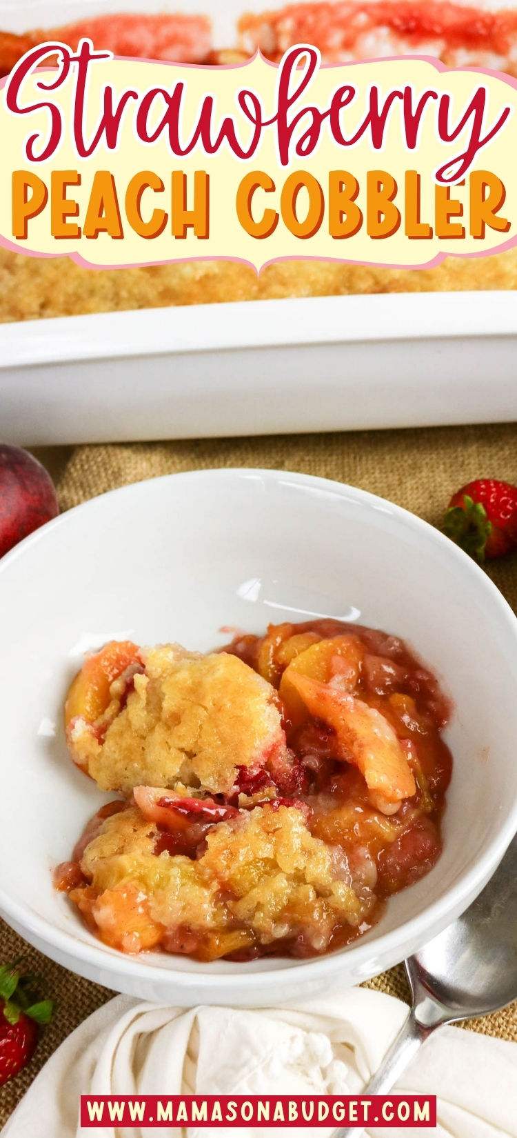 A bowl of strawberry peach cobbler with a spoon, sitting on a table next to a white baking dish and fresh fruit.