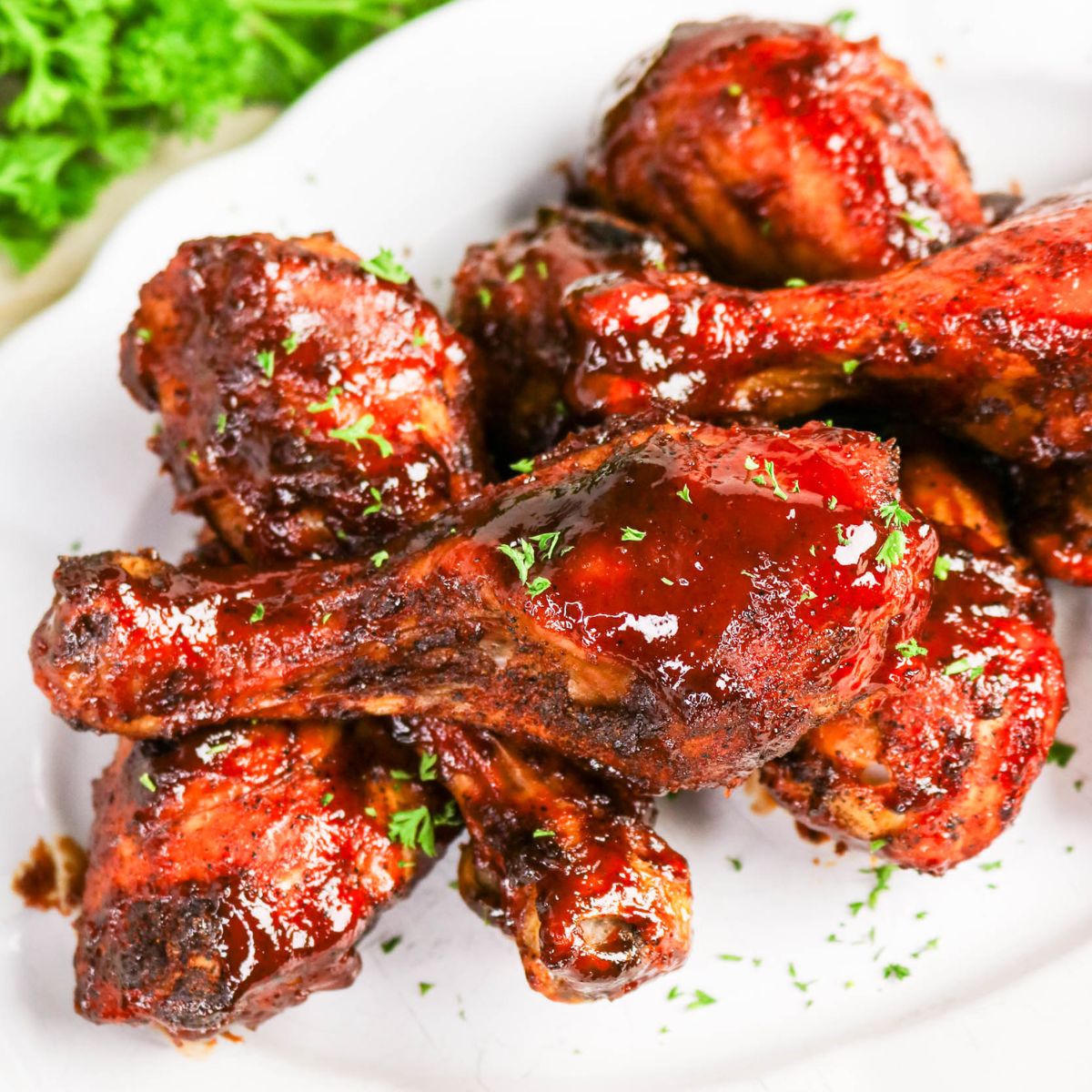 A plate of glazed barbecue chicken drumsticks garnished with chopped parsley, served on a white dish.
