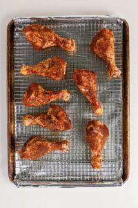Eight raw, seasoned chicken drumsticks arranged on a wire rack over a foil-lined baking sheet, ready for cooking.