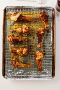 Eight seasoned chicken drumsticks on a wire rack over a foil-lined baking sheet, ready to be cooked or just finished baking.