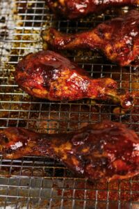 Barbecued chicken drumsticks with a glossy sauce on a wire rack over a baking sheet.